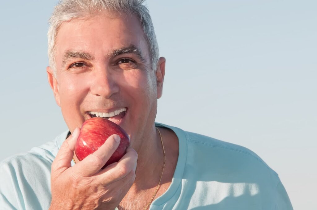 man eating apple after successful dental implant recovery